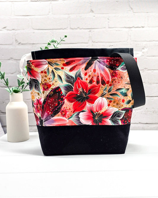 Handgenähte Projekttasche mit leuchtend roten Blüten und Schmetterlingen auf dunklem Grund mit schwarzem Boden. Handmade in Bayern von Nadelmikado.