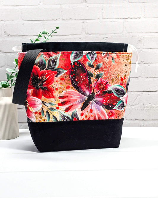 Handgenähte Projekttasche mit leuchtend roten Blüten und Schmetterlingen auf dunklem Grund mit schwarzem Boden. Handmade in Bayern von Nadelmikado.