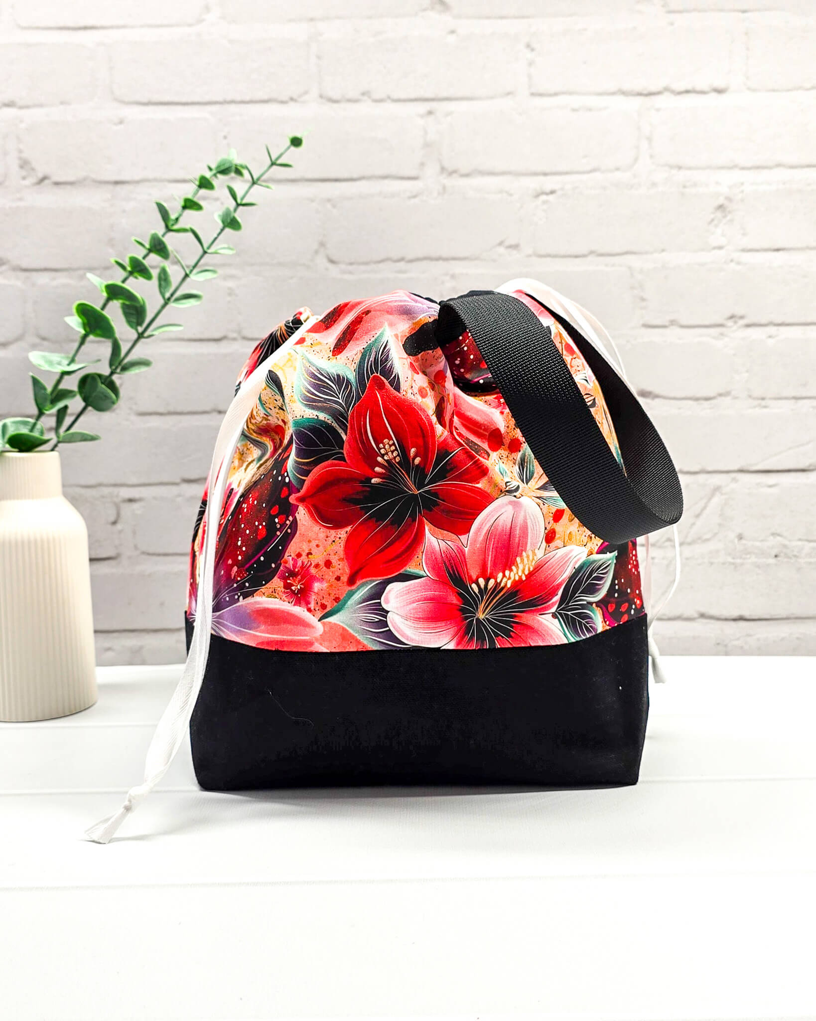 Handgenähte Projekttasche mit leuchtend roten Blüten und Schmetterlingen auf dunklem Grund mit schwarzem Boden. Handmade in Bayern von Nadelmikado.