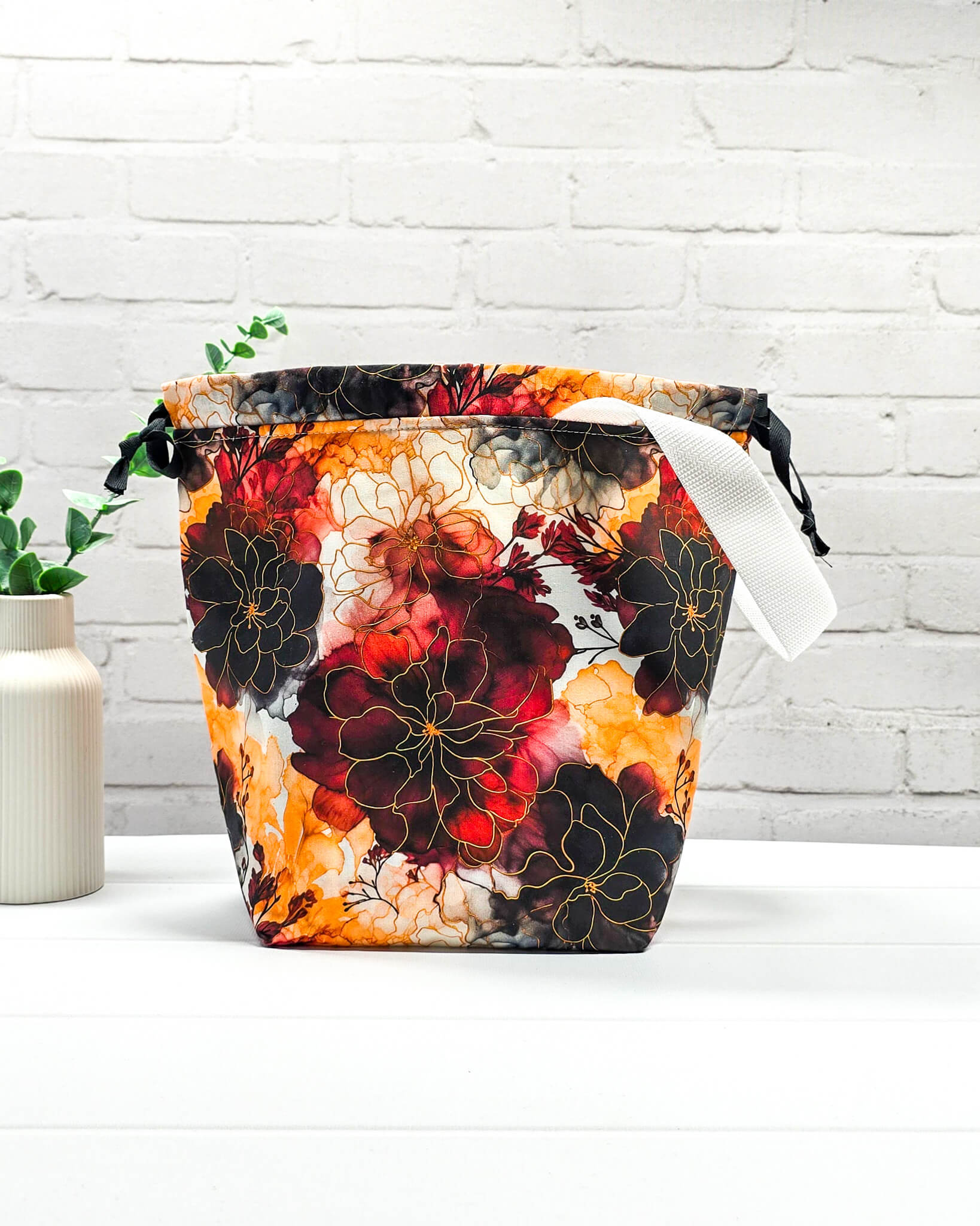 Projekttasche Tuva M aus Baumwolle mit weinroten und senfgelben Aquarell-Blumen, schwarzem Kordelzug und heller Schlaufe. Handgenäht in Bayern von Nadelmikado. 