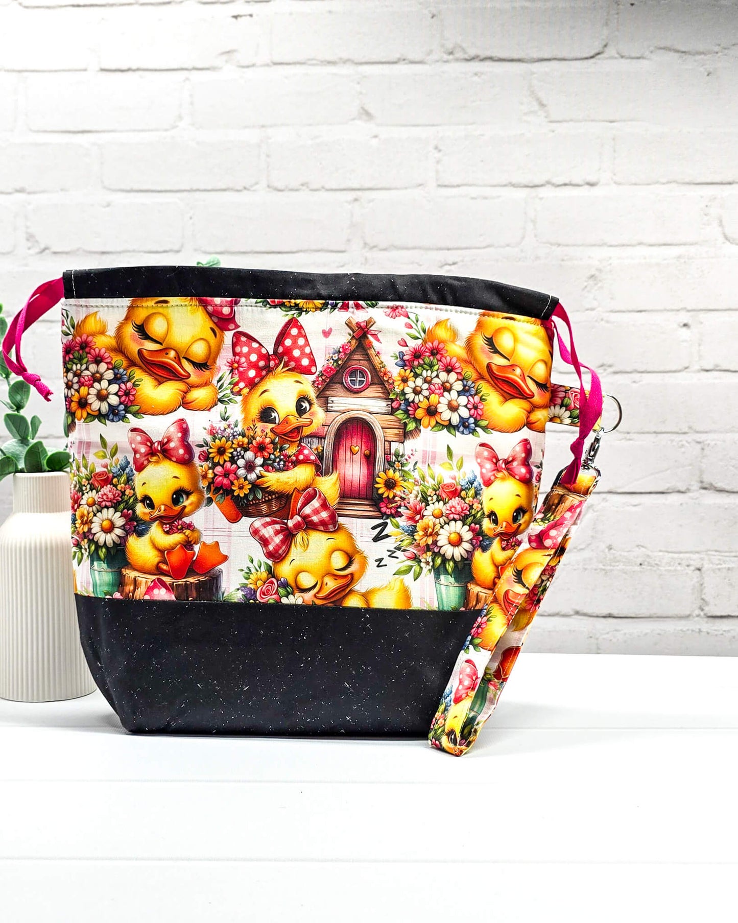 Projekttasche Tuva M aus Baumwolle mit gelben Küken, Blumenmotiven, pinken Zugkordeln und abnehmbarer Handschlaufe. Handgenäht in Bayern von Nadelmikado. 