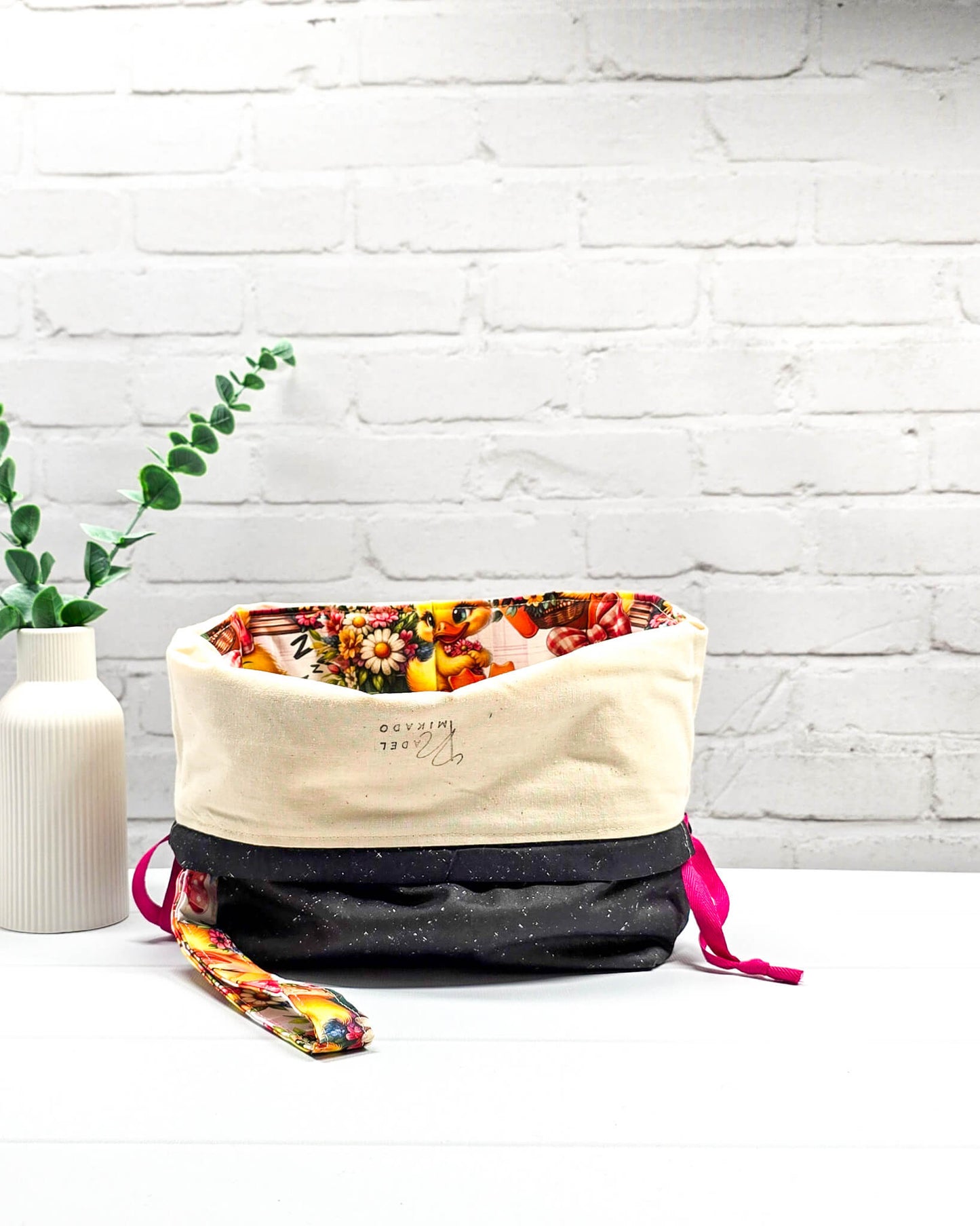 Projekttasche Tuva M aus Baumwolle mit gelben Küken, Blumenmotiven, pinken Zugkordeln und abnehmbarer Handschlaufe. Handgenäht in Bayern von Nadelmikado. 