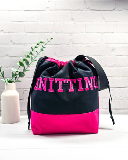 Bestickte Projekttasche Tuva M aus schwarzem und pinkem Canvas-Stoff mit pinkem Schriftzug KNITTING, schwarzem Kordelzug und schwarzem Tragegurt. Bietet Platz für 400g Wolle. Handgenäht in Bayern von Nadelmikado.