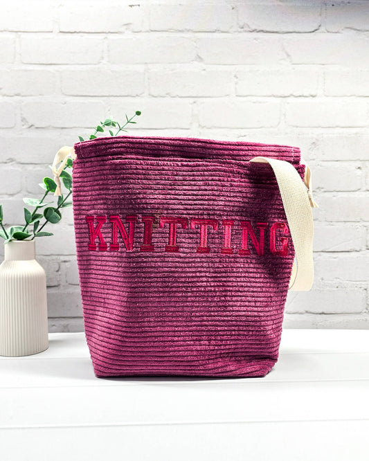 Bestickte Projekttasche Tuva M aus beerefarbenem Breitcord mit dem Schriftzug KNITTING, Kordelzug und cremefarbenem Tragegurt. Bietet Platz für 400g Wolle und schützt das Strickzeug vor Verheddern. Handgenäht in Bayern von Nadelmikado.