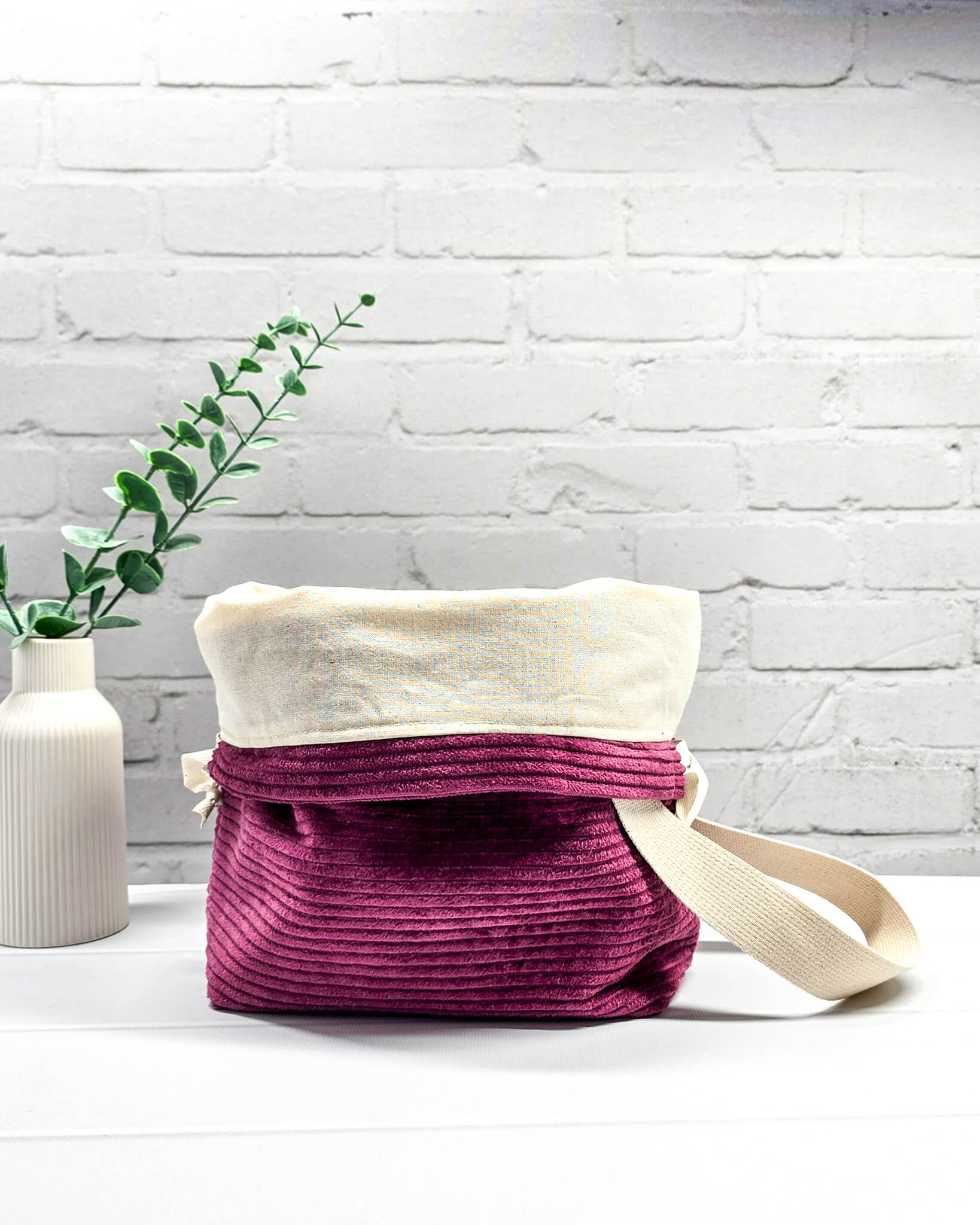 Bestickte Projekttasche Tuva M aus beerefarbenem Breitcord mit dem Schriftzug KNITTING, Kordelzug und cremefarbenem Tragegurt. Bietet Platz für 400g Wolle und schützt das Strickzeug vor Verheddern. Handgenäht in Bayern von Nadelmikado.