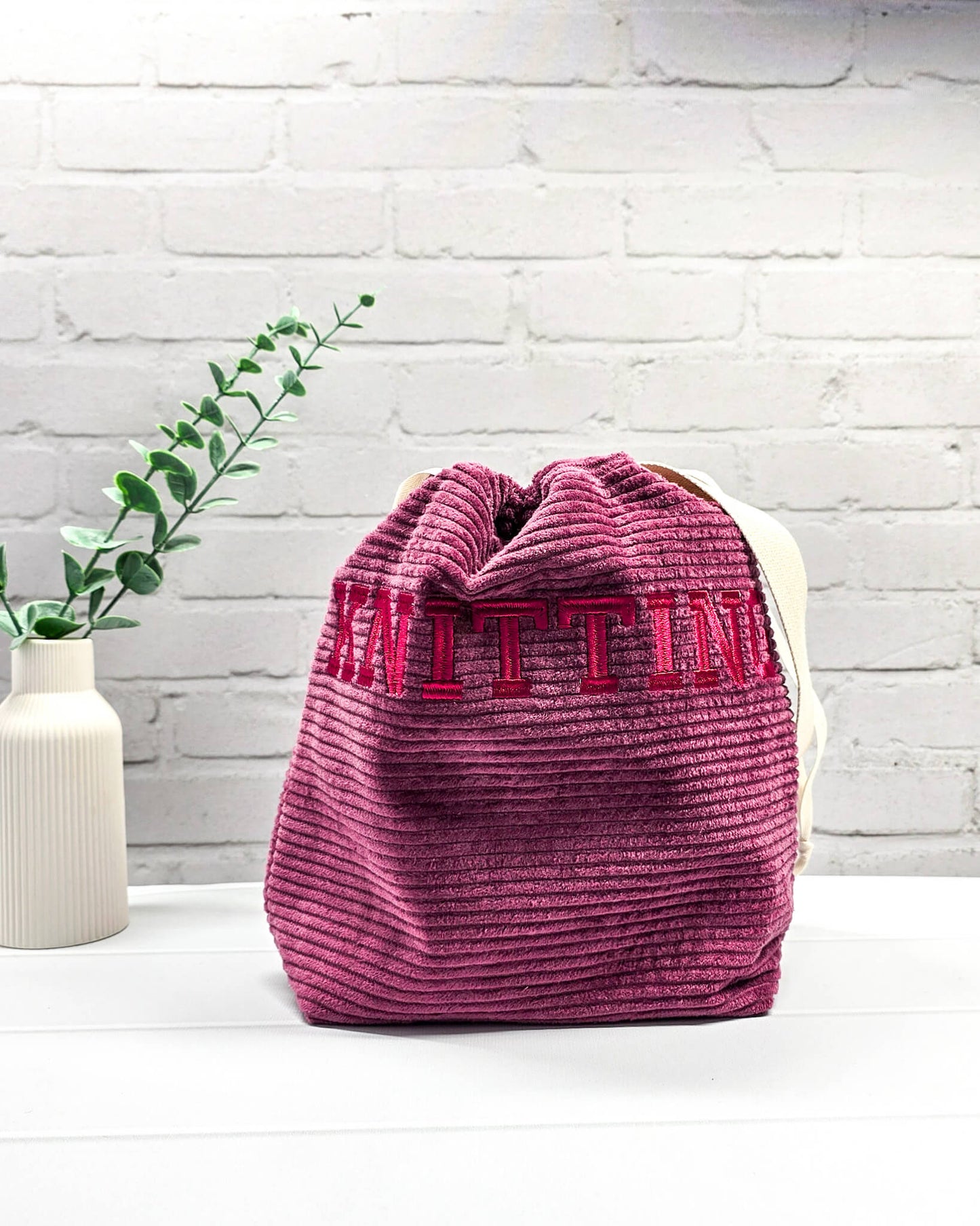 Bestickte Projekttasche Tuva M aus beerefarbenem Breitcord mit dem Schriftzug KNITTING, Kordelzug und cremefarbenem Tragegurt. Bietet Platz für 400g Wolle und schützt das Strickzeug vor Verheddern. Handgenäht in Bayern von Nadelmikado.