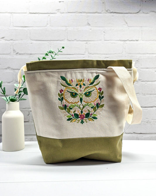 Projekttasche Tuva M aus hellem Canvas mit gesticktem Eulenmotiv, olivgrünem Boden, Kordelzug und Tragegurt. Bietet Platz für 400g Wolle. Handgenäht in Bayern von Nadelmikado.
