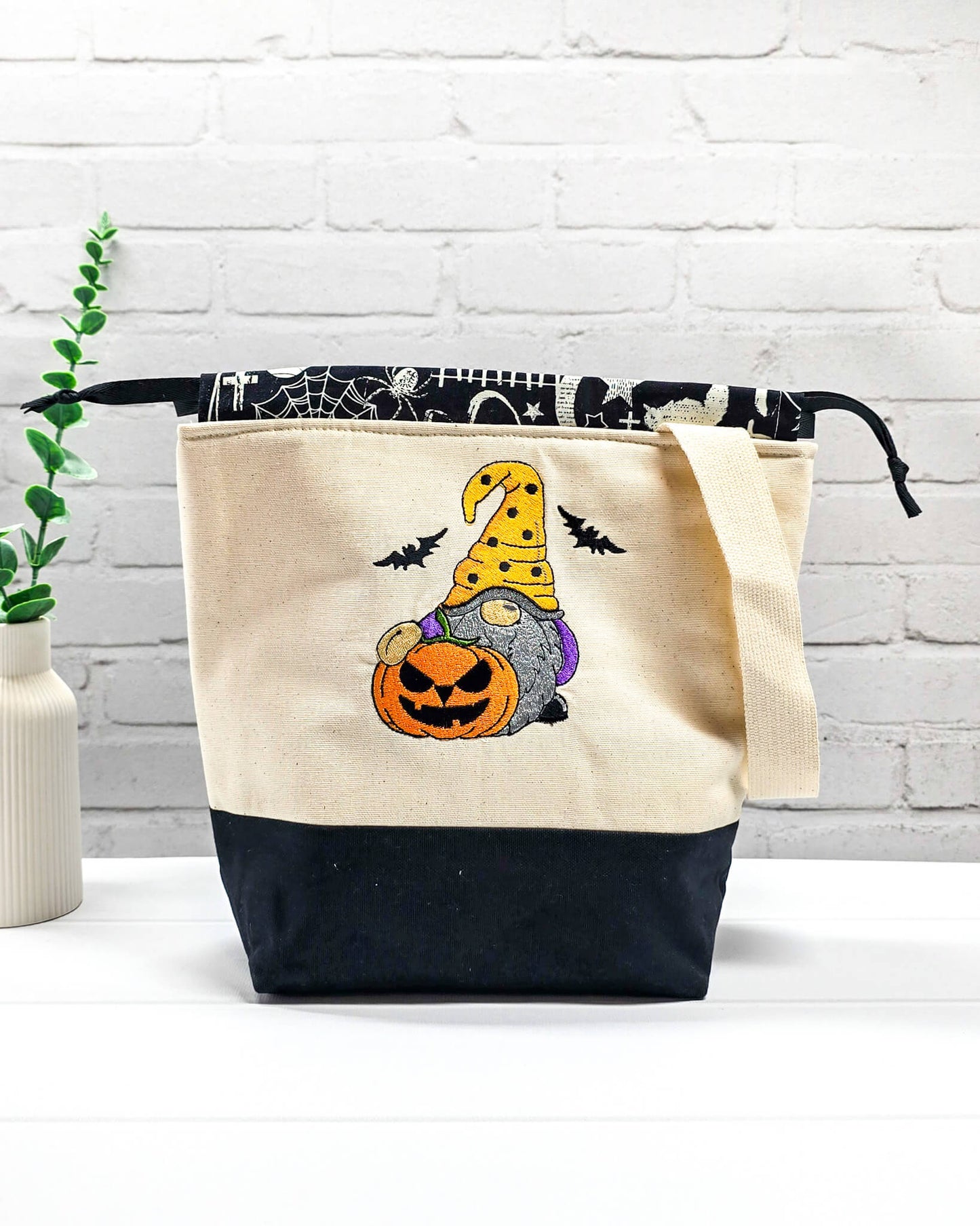 Projekttasche Tuva M aus hellem Canvas mit gesticktem Halloween Gnom, Kürbis und schwarzem Kordelzugkragen. Handgenäht in Bayern von Nadelmikado.