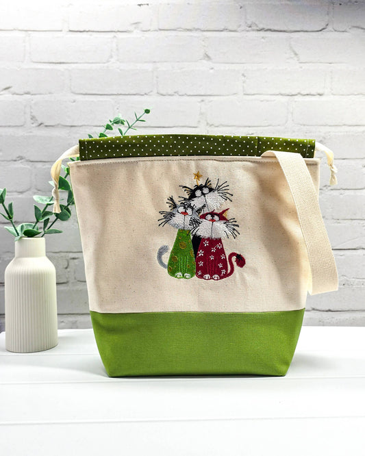 Projekttasche Tuva M aus hellem Canvas und grünem Stoff mit gesticktem Katzen-Trio (drei bunte Katzen mit Schnurrhaaren), grün weiß gepunktetem Kordelzug und cremefarbenem Tragegurt. Bietet Platz für 400g Wolle und schützt das Strickzeug vor Verheddern. Handgenäht in Bayern von Nadelmikado.