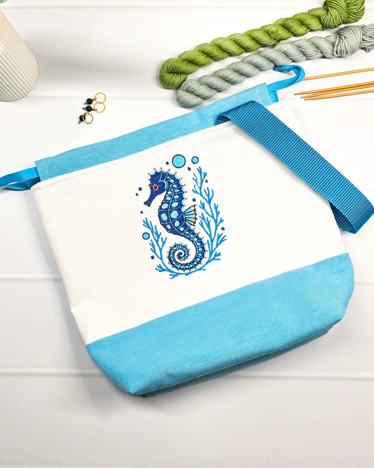 Projekttasche Tuva M aus hellem Canvas und hellblauem Stoff mit blau gesticktem Seepferdchen-Motiv im Korallenkranz, Kordelzug und blauem Tragegurt. Bietet Platz für 400g Wolle und schützt das Strickzeug vor Verheddern. Handgenäht in Bayern von Nadelmikado.