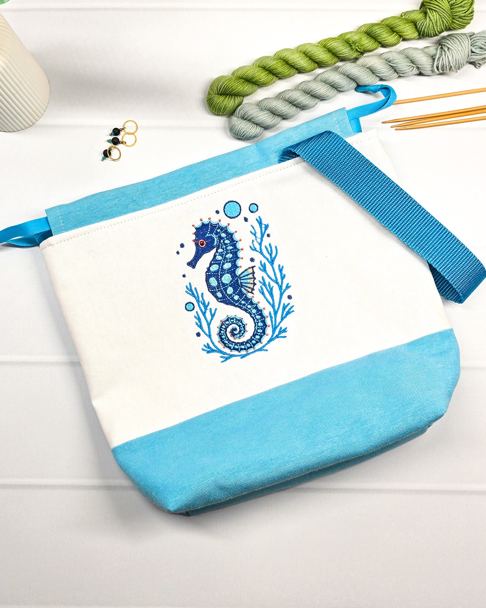 Projekttasche Tuva M aus hellem Canvas und hellblauem Stoff mit blau gesticktem Seepferdchen-Motiv im Korallenkranz, Kordelzug und blauem Tragegurt. Bietet Platz für 400g Wolle und schützt das Strickzeug vor Verheddern. Handgenäht in Bayern von Nadelmikado.