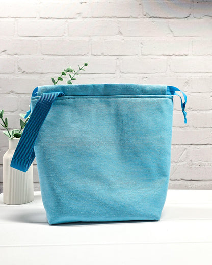 Projekttasche Tuva M aus hellem Canvas und hellblauem Stoff mit blau gesticktem Seepferdchen-Motiv im Korallenkranz, Kordelzug und blauem Tragegurt. Bietet Platz für 400g Wolle und schützt das Strickzeug vor Verheddern. Handgenäht in Bayern von Nadelmikado.