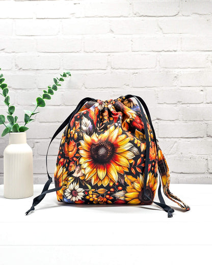 Projekttasche Tuva M aus schwarzem Baumwollstoff mit großen Sonnenblumen, Herbstlaub, Innentaschen und abnehmbarer Trageschlaufe. Handgenäht in Bayern von Nadelmikado. 