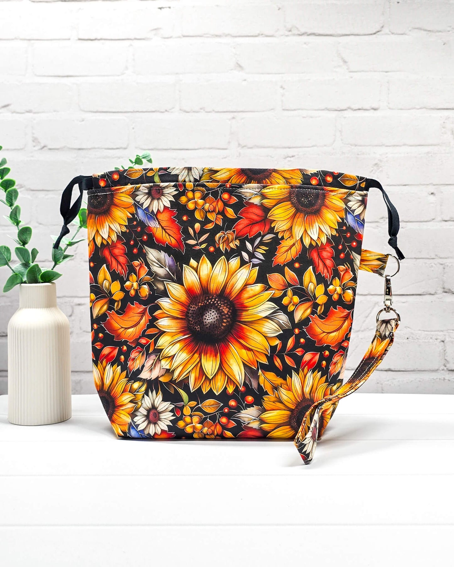 Projekttasche Tuva M aus schwarzem Baumwollstoff mit großen Sonnenblumen, Herbstlaub, Innentaschen und abnehmbarer Trageschlaufe. Handgenäht in Bayern von Nadelmikado. 