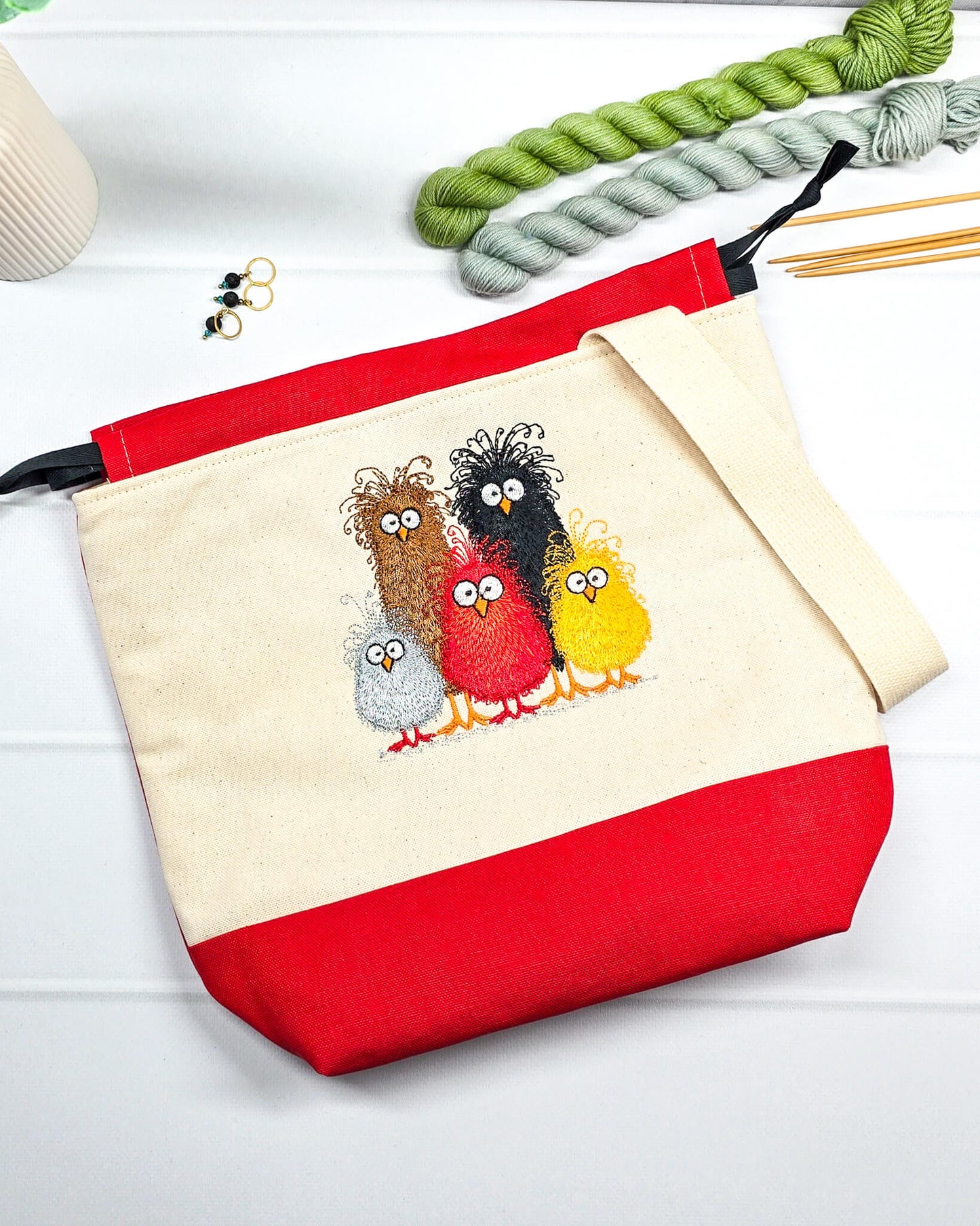 Projekttasche Tuva M aus hellem Canvas und rotem Stoff mit fünf bunt gestickten, strubbeligen Vögeln, schwarzem Kordelzug und cremefarbenem Tragegurt. Bietet Platz für 400g Wolle und schützt das Strickzeug vor Verheddern. Handgenäht in Bayern von Nadelmikado.