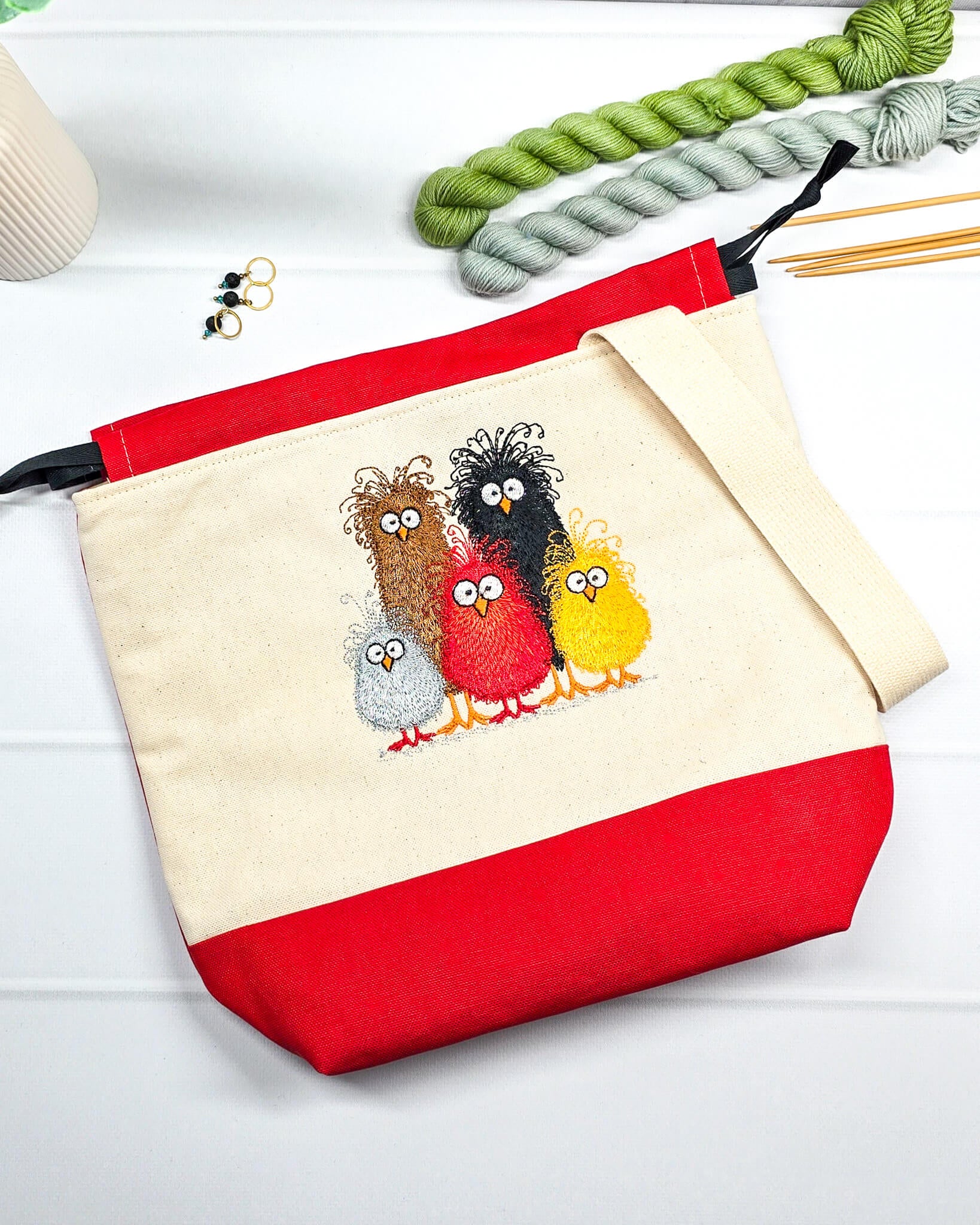 Projekttasche Tuva M aus hellem Canvas und rotem Stoff mit fünf bunt gestickten, strubbeligen Vögeln, schwarzem Kordelzug und cremefarbenem Tragegurt. Bietet Platz für 400g Wolle und schützt das Strickzeug vor Verheddern. Handgenäht in Bayern von Nadelmikado.