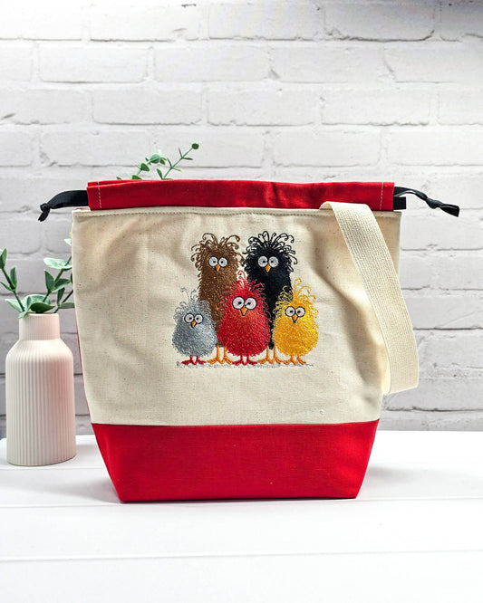 Projekttasche Tuva M aus hellem Canvas und rotem Stoff mit fünf bunt gestickten, strubbeligen Vögeln, schwarzem Kordelzug und cremefarbenem Tragegurt. Bietet Platz für 400g Wolle und schützt das Strickzeug vor Verheddern. Handgenäht in Bayern von Nadelmikado.