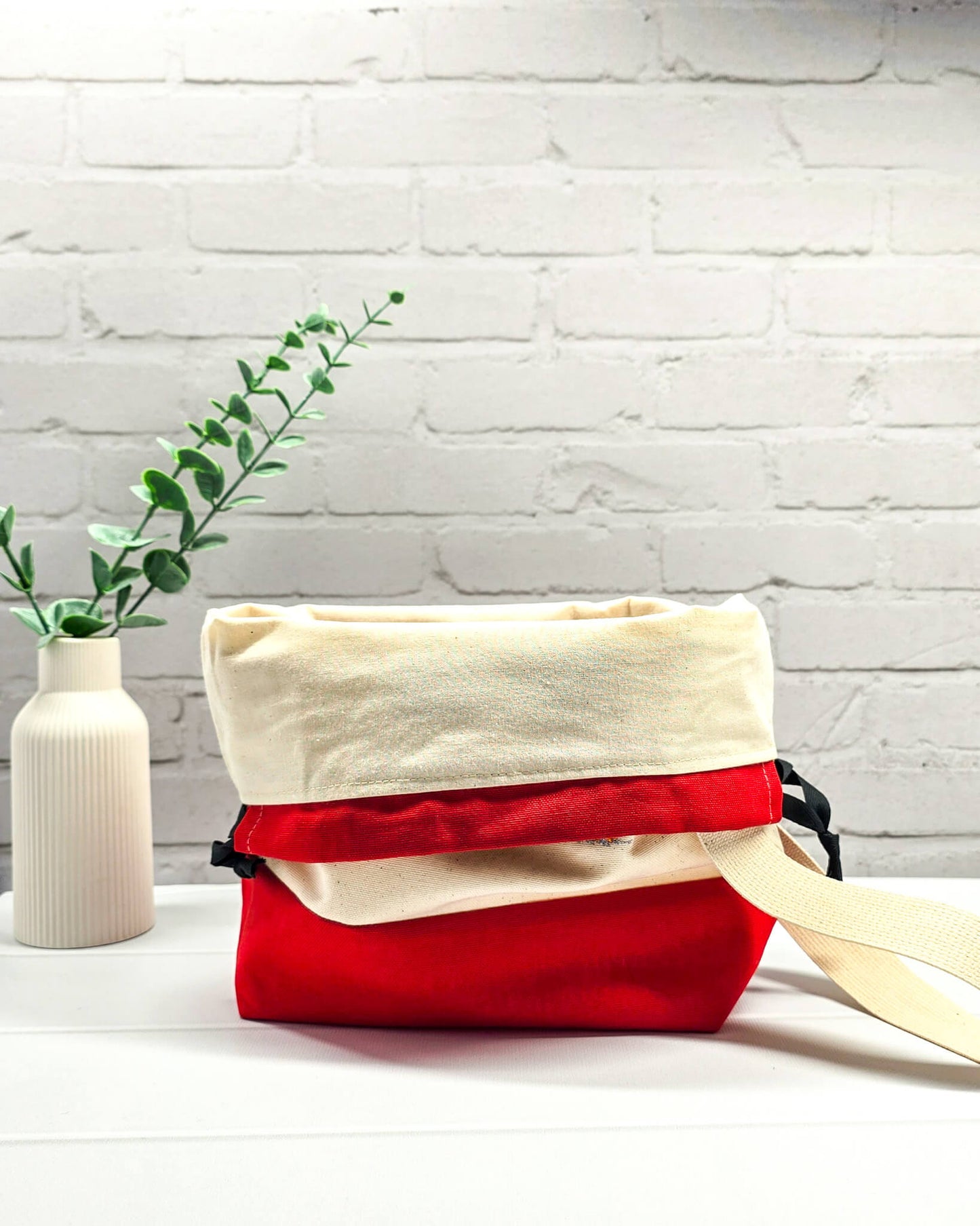 Projekttasche Tuva M aus hellem Canvas und rotem Stoff mit fünf bunt gestickten, strubbeligen Vögeln, schwarzem Kordelzug und cremefarbenem Tragegurt. Bietet Platz für 400g Wolle und schützt das Strickzeug vor Verheddern. Handgenäht in Bayern von Nadelmikado.