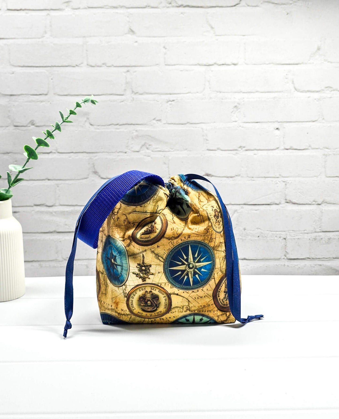 Handgenähte Projekttasche Tuva S von Nadelmikado mit Kompass-Motiv und Vintage-Weltkarte, seitlicher blauer Tragegurt, stehend auf weißem Grund.
