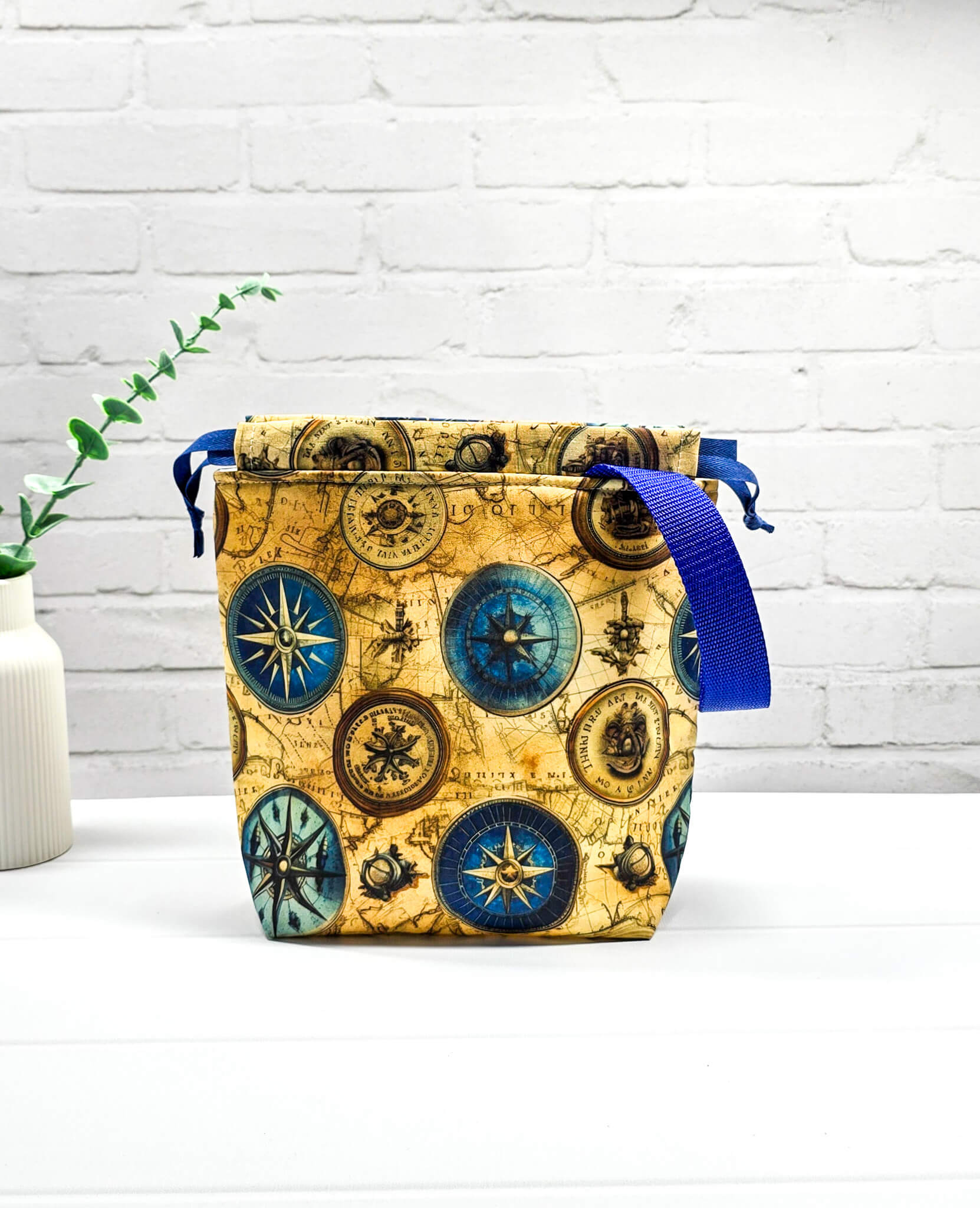 Handgenähte Projekttasche Tuva S von Nadelmikado mit Kompass-Motiv und Vintage-Weltkarte, seitlicher blauer Tragegurt, stehend auf weißem Grund.