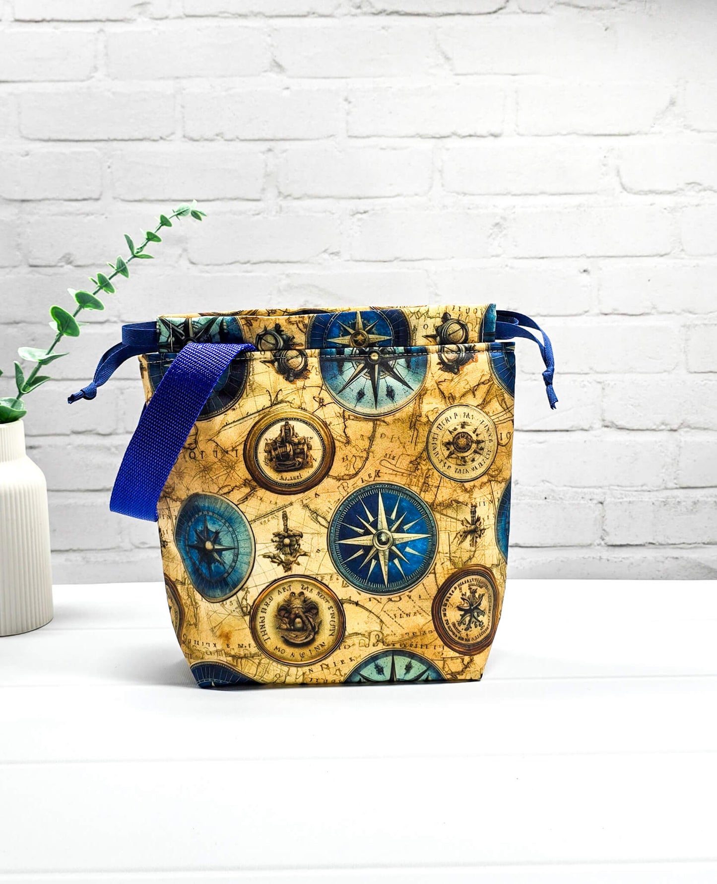 Handgenähte Projekttasche Tuva S von Nadelmikado mit Kompass-Motiv und Vintage-Weltkarte, seitlicher blauer Tragegurt, stehend auf weißem Grund.