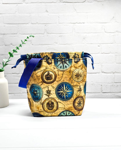 Handgenähte Projekttasche Tuva S von Nadelmikado mit Kompass-Motiv und Vintage-Weltkarte, seitlicher blauer Tragegurt, stehend auf weißem Grund.