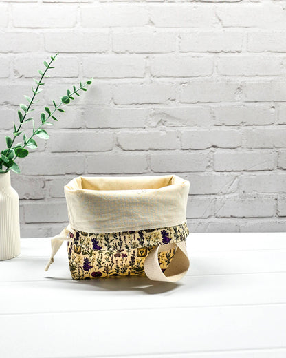 Kleine Projekttasche Tuva S mit einem breiten hellen Trageriemen und botanischem Kräuterküche-Muster auf beigem Grund. Handgenäht in Bayern von Nadelmikado.