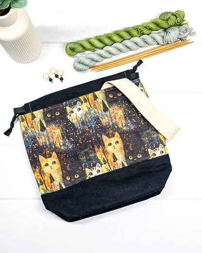 Kleine Handarbeitstasche mit Katzen-Motiv auf dunklem Grund, schwarzem Boden, schwarzem Kordelzug und hellem Tragegurt. Für 200g Wolle. Handgenäht in Bayern von Nadelmikado.