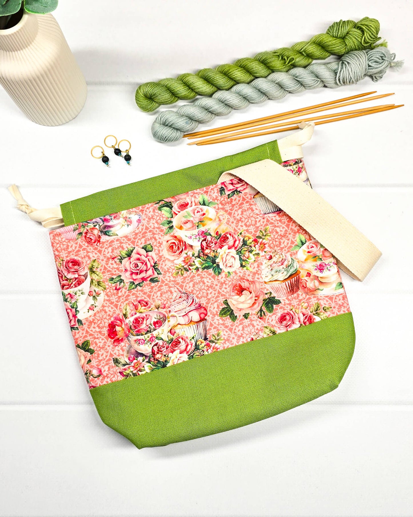 Handgenähter Projektbeutel mit Rosen- und Teetassen-Motiv auf rosa Mustergrund, grünem Boden, cremefarbenem Kordelzug und Tragegurt. Für 200g Wolle. Handgenäht in Bayern von Nadelmikado.