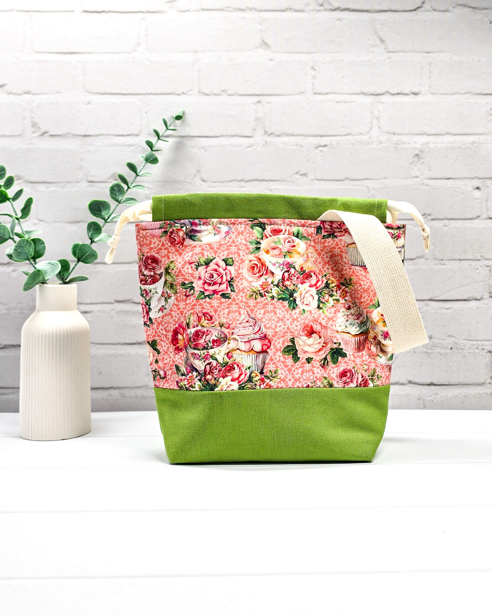 Handgenähter Projektbeutel mit Rosen- und Teetassen-Motiv auf rosa Mustergrund, grünem Boden, cremefarbenem Kordelzug und Tragegurt. Für 200g Wolle. Handgenäht in Bayern von Nadelmikado.