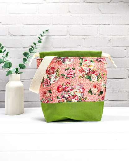 Handgenähter Projektbeutel mit Rosen- und Teetassen-Motiv auf rosa Mustergrund, grünem Boden, cremefarbenem Kordelzug und Tragegurt. Für 200g Wolle. Handgenäht in Bayern von Nadelmikado.