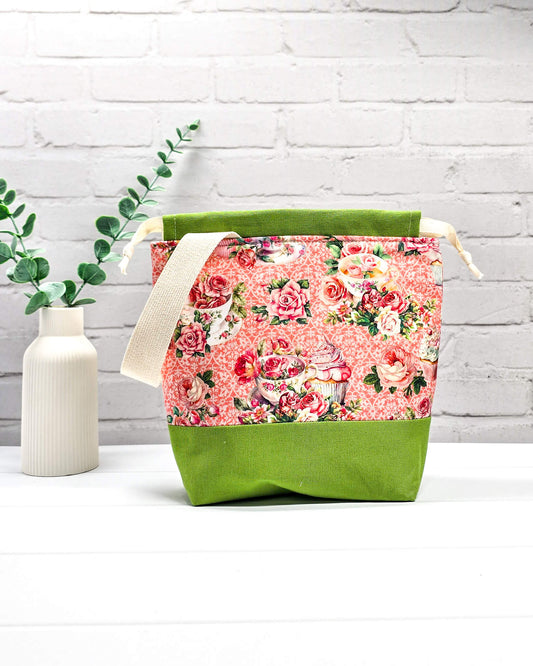 Handgenähter Projektbeutel mit Rosen- und Teetassen-Motiv auf rosa Mustergrund, grünem Boden, cremefarbenem Kordelzug und Tragegurt. Für 200g Wolle. Handgenäht in Bayern von Nadelmikado.