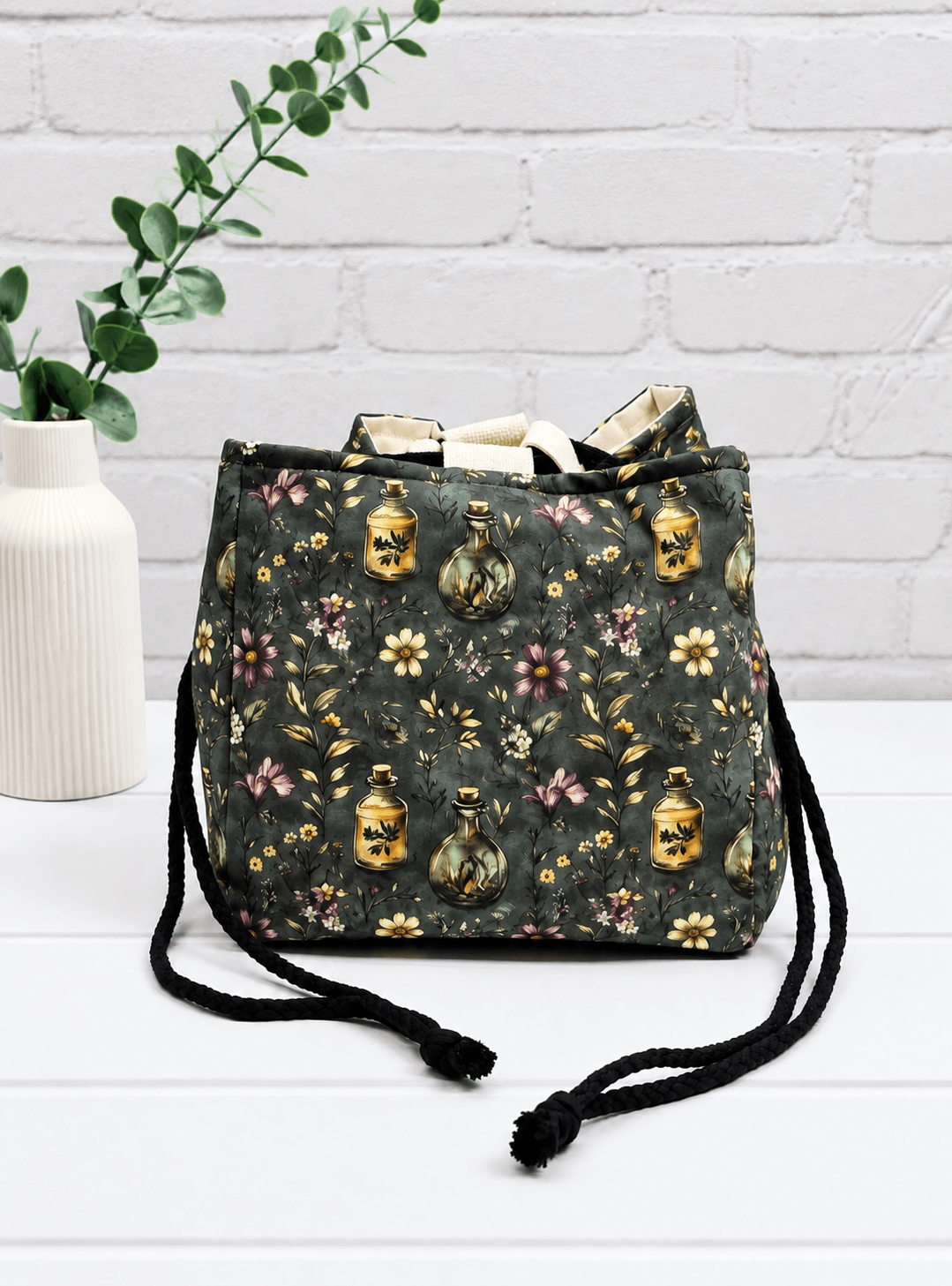 Rice Bag mit Blüten, Zweigen und Apothekerfläschchen auf dunklem Stoff. Handgenäht in Bayern von NadelMikado.