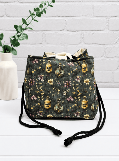 Rice Bag mit Blüten, Zweigen und Apothekerfläschchen auf dunklem Stoff. Handgenäht in Bayern von NadelMikado.