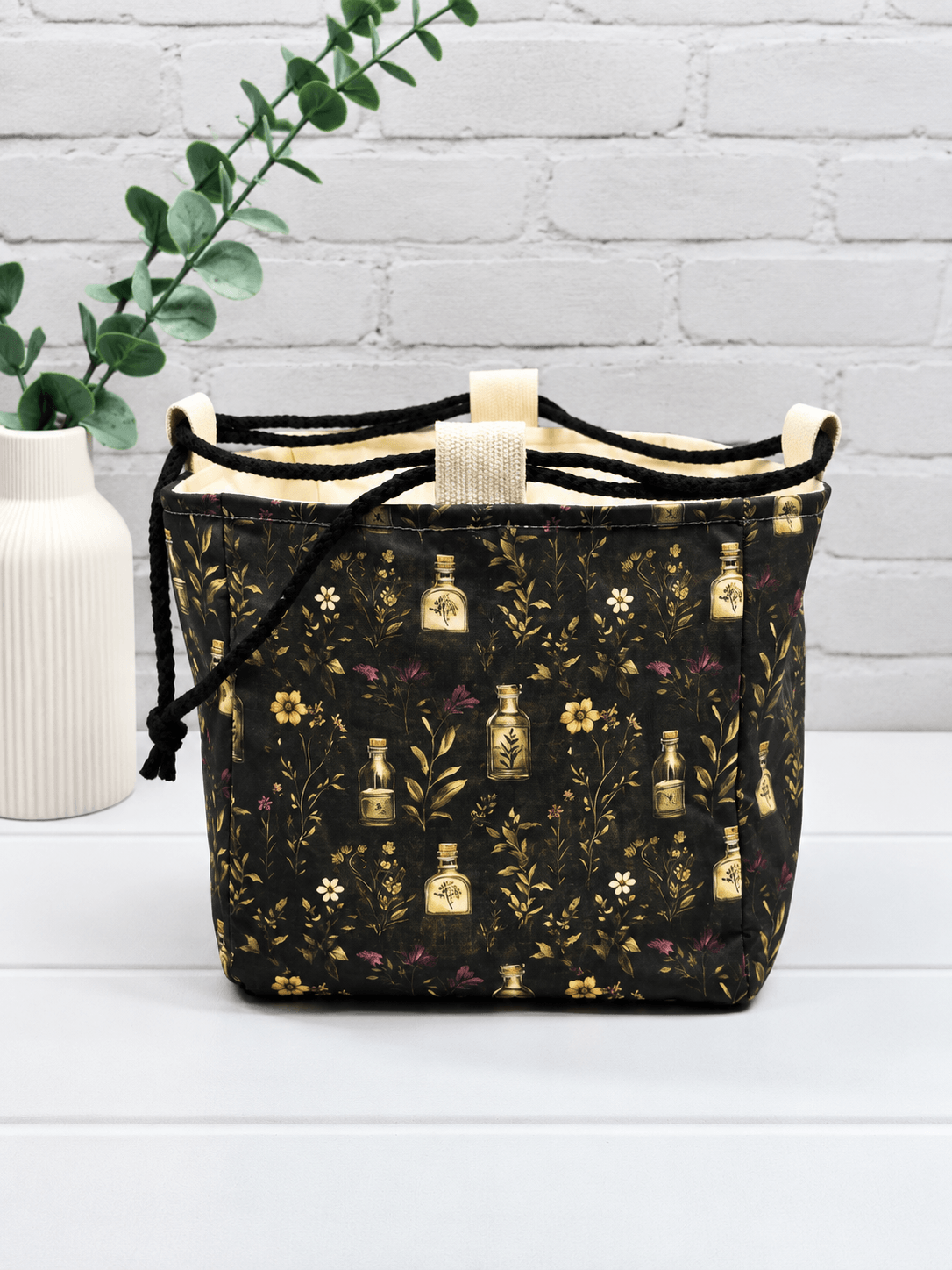 Rice Bag mit botanischem Muster aus Fläschchen, Blüten und Zweigen auf dunklem Stoff. Handgenäht in Bayern von NadelMikado.