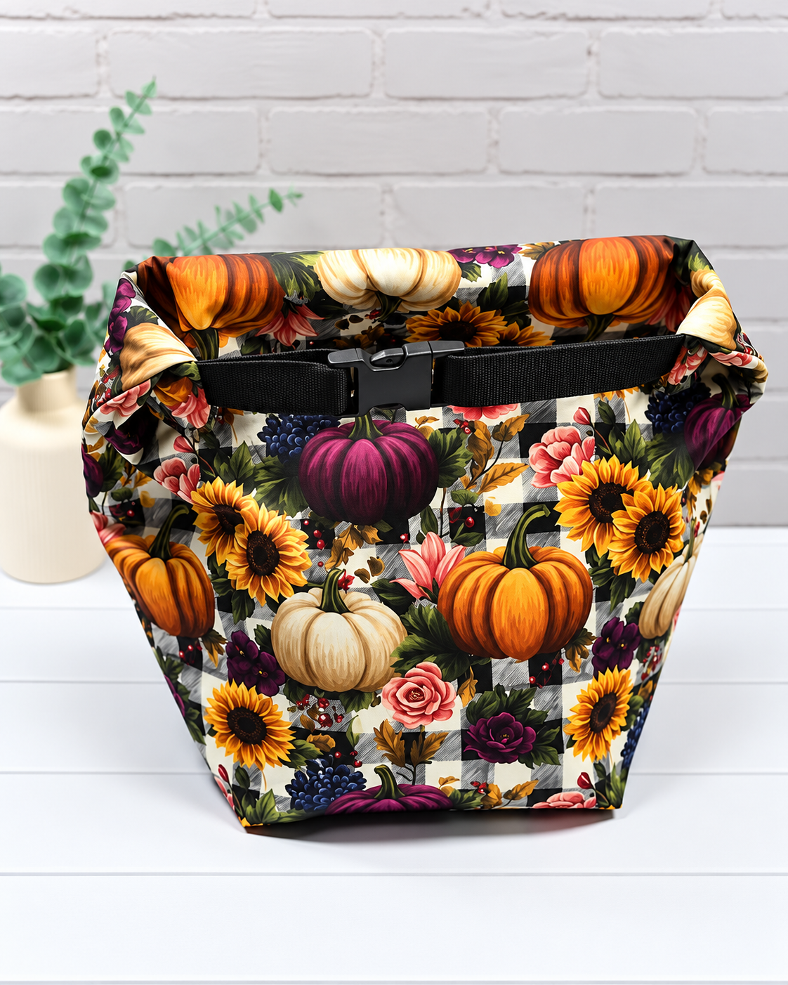 Rolltop-Projekttasche Rika mit bunten Kürbissen, Sonnenblumen und Rosen auf schwarz-weißem Karomuster, seitlichen Gurten und Steckverschluss. Handgenäht in Bayern von Nadelmikado.