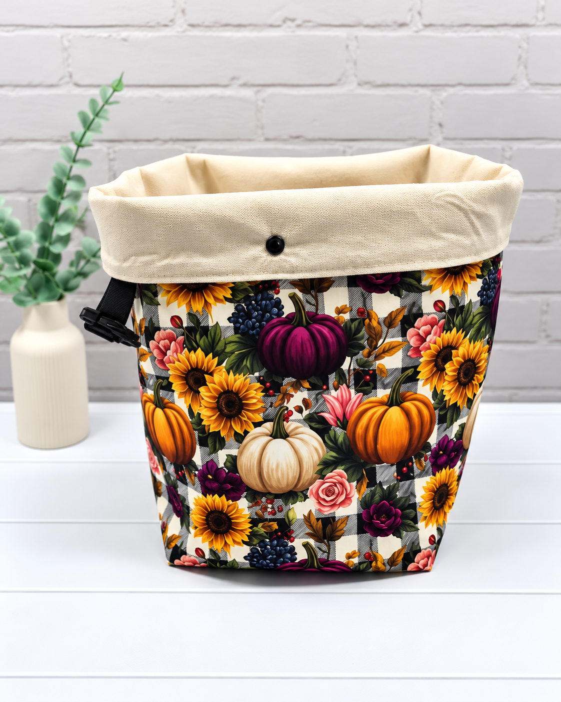 Rolltop-Projekttasche Rika mit bunten Kürbissen, Sonnenblumen und Rosen auf schwarz-weißem Karomuster, seitlichen Gurten und Steckverschluss. Handgenäht in Bayern von Nadelmikado.