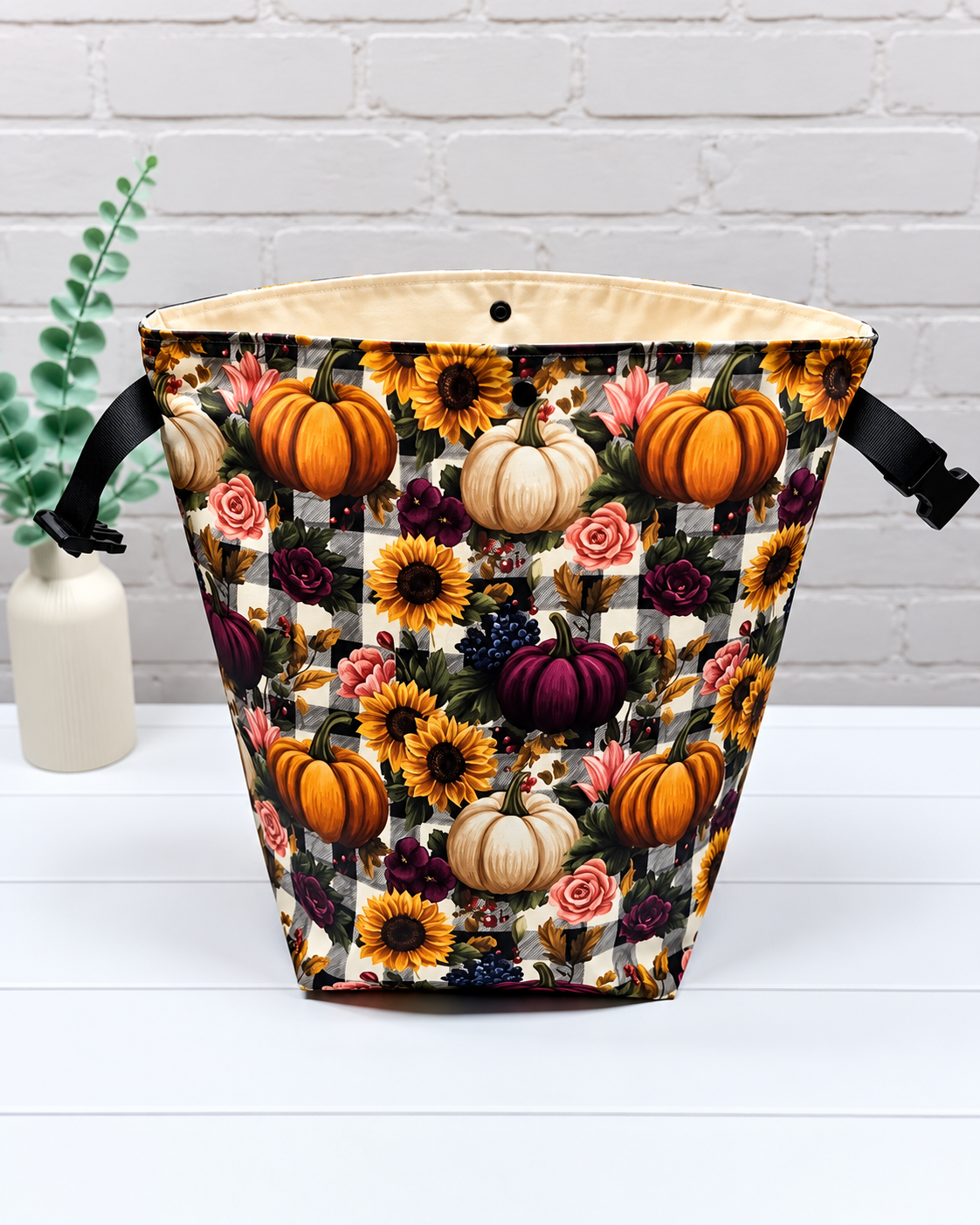 Rolltop-Projekttasche Rika mit bunten Kürbissen, Sonnenblumen und Rosen auf schwarz-weißem Karomuster, seitlichen Gurten und Steckverschluss. Handgenäht in Bayern von Nadelmikado.