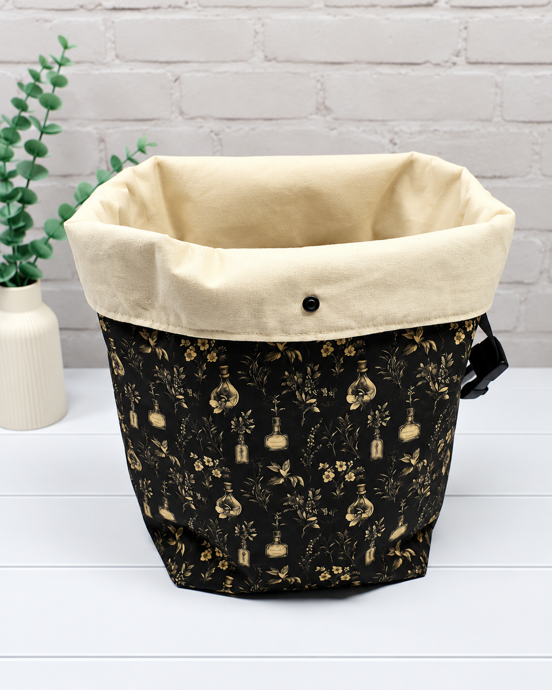 Rolltop-Projekttasche Rika mit kleinen Fläschchen, Blüten und feinen Ranken in Beige auf schwarzem Hintergrund. Handgenäht in Bayern von Nadelmikado.