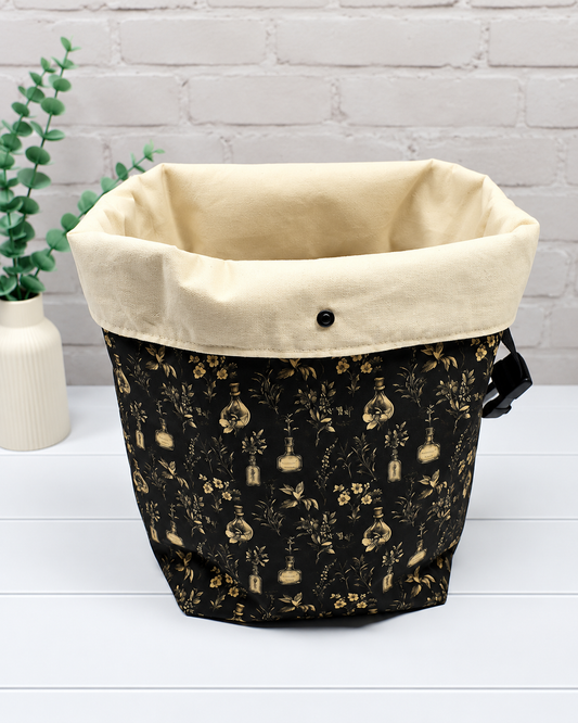 Rolltop-Projekttasche Rika mit kleinen Fläschchen, Blüten und feinen Ranken in Beige auf schwarzem Hintergrund. Handgenäht in Bayern von Nadelmikado.