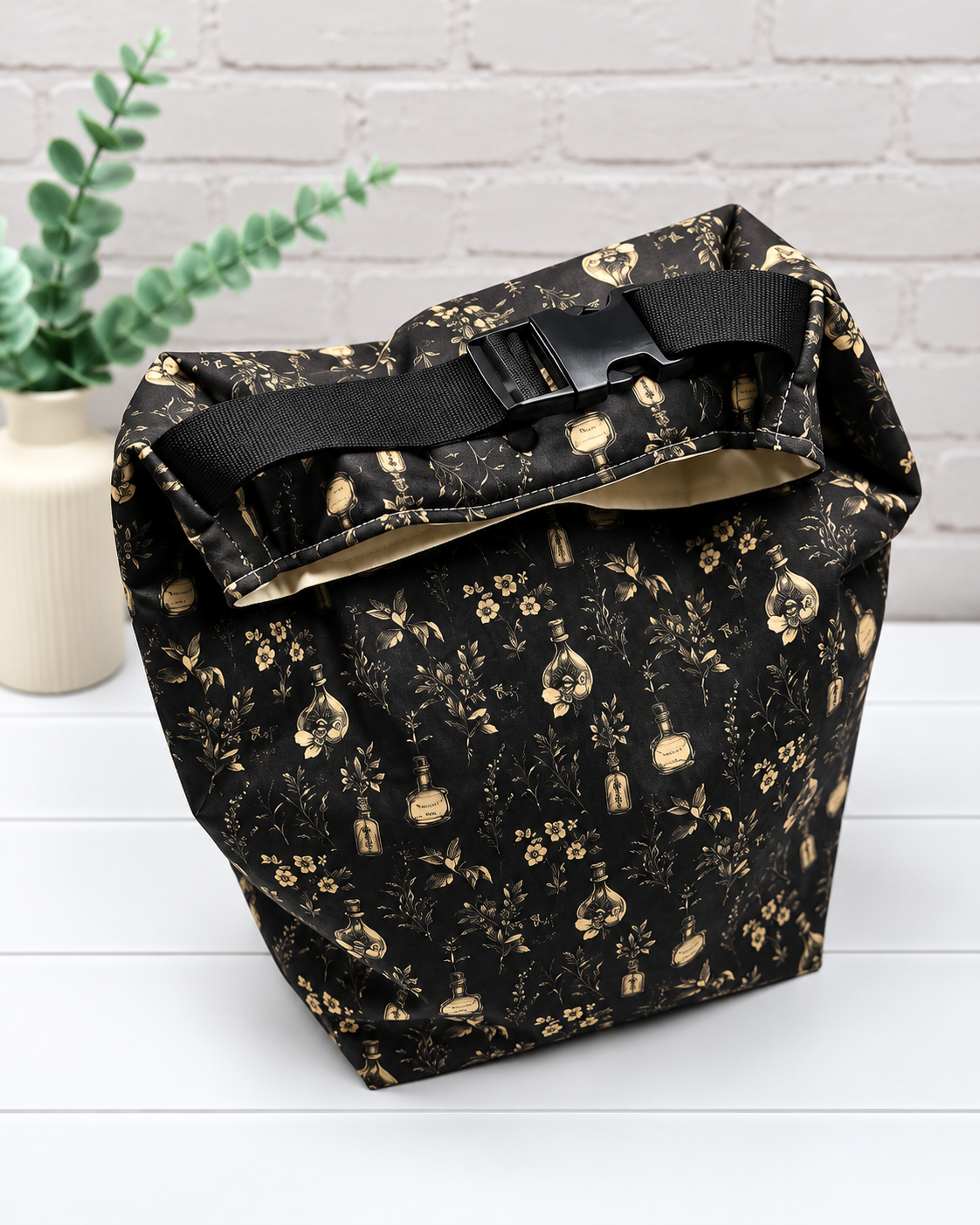 Rolltop-Projekttasche Rika mit kleinen Fläschchen, Blüten und feinen Ranken in Beige auf schwarzem Hintergrund. Handgenäht in Bayern von Nadelmikado.