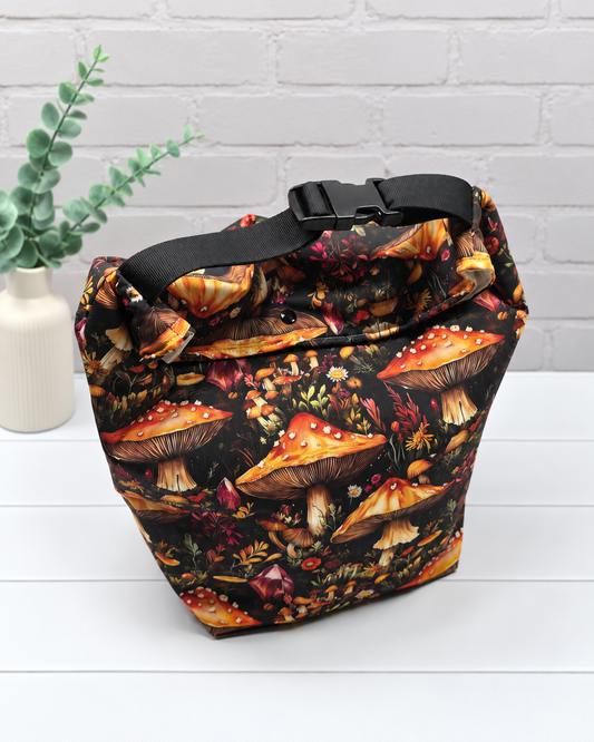 Rolltop-Projekttasche Rika mit orange-roten Fliegenpilzen, roten Kristallen und herbstlichen Waldpflanzen auf schwarzem Stoff. Handgenäht in Bayern von Nadelmikado.