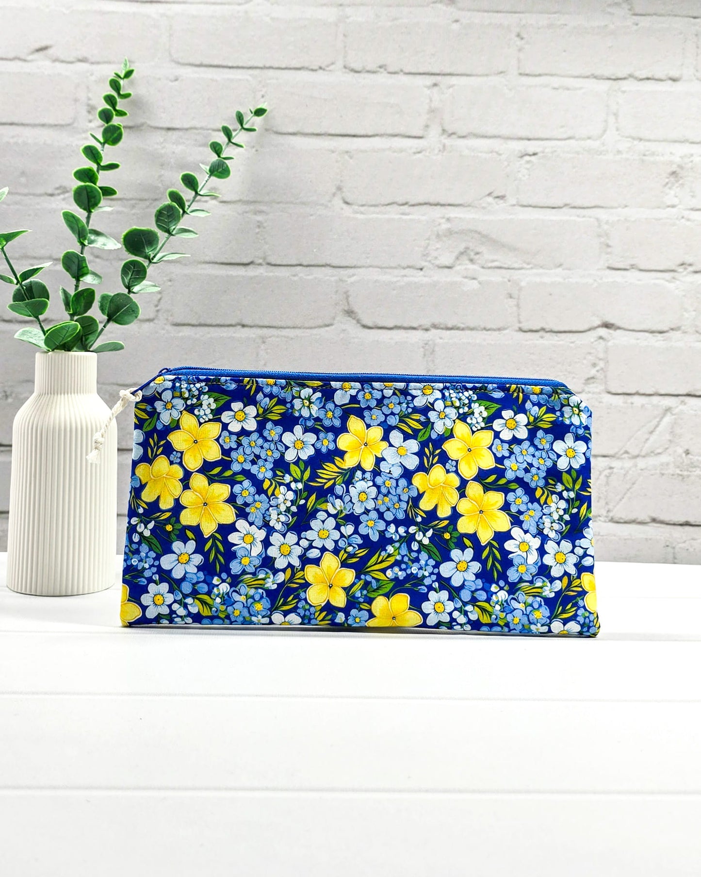 Flache Reißverschlusstasche mit blauem Reißverschluss, hellem Kordel-Zipper und buntem Blumenmuster mit gelben und blauen Blüten. Handgenäht in Bayern von Nadelmikado.