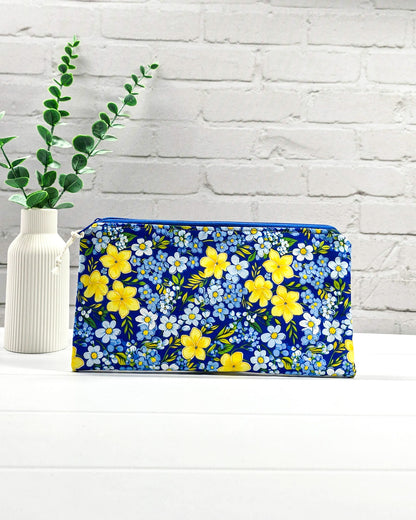 Flache Reißverschlusstasche mit blauem Reißverschluss, hellem Kordel-Zipper und buntem Blumenmuster mit gelben und blauen Blüten. Handgenäht in Bayern von Nadelmikado.