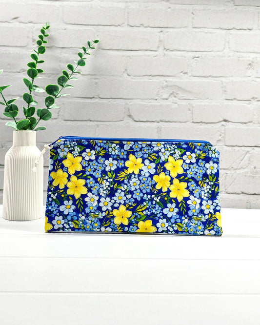 Flache Reißverschlusstasche mit blauem Reißverschluss, hellem Kordel-Zipper und buntem Blumenmuster mit gelben und blauen Blüten. Handgenäht in Bayern von Nadelmikado.