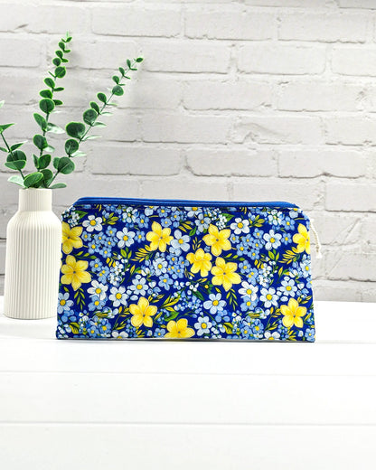 Flache Reißverschlusstasche mit blauem Reißverschluss, hellem Kordel-Zipper und buntem Blumenmuster mit gelben und blauen Blüten. Handgenäht in Bayern von Nadelmikado.