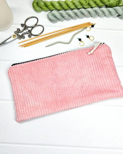 Kleine altrosafarbene Reißverschlusstasche aus Cord-Stoff für Strickzubehör, liegend auf weißem Untergrund mit einer Schere, Garnsträngen und Holznadeln. Handgenäht in Bayern von Nadelmikado.