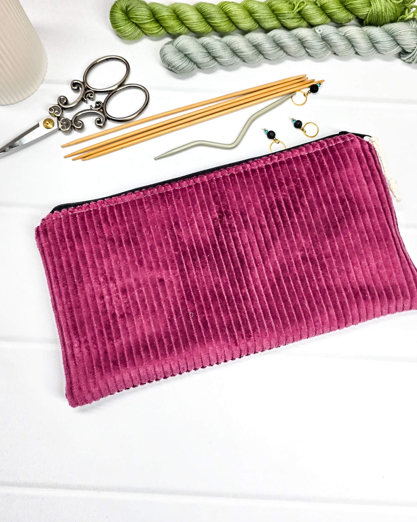 Kleine Reißverschlusstasche aus beerenfarbenem Cord-Stoff auf hellem Untergrund mit Strickzubehör. Handgenäht in Bayern von Nadelmikado. 