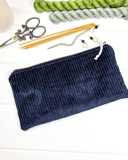 Kleine Reißverschlusstasche aus dunkelblauem Cord-Stoff für Strickzubehör, flach liegend auf weißem Untergrund mit Schere, Garn und Nadeln. Handgenäht in Bayern von Nadelmikado.
