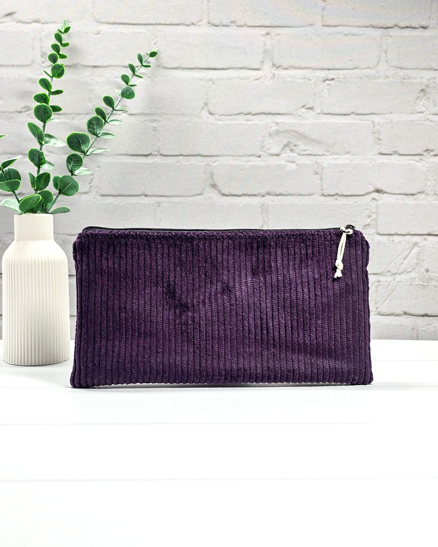 Kleine lila Reißverschlusstasche aus Cord-Stoff für Strickzubehör, flach liegend auf weißem Untergrund mit einer Schere, Garnsträngen und Holznadeln. Handgenäht in Bayern von Nadelmikado.